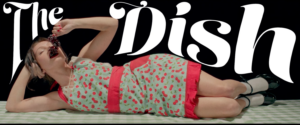 Person laying on table eating grapes with text above them saying "The Dish"